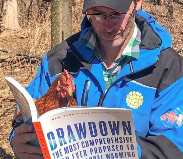 Man reads the book Drawdown with a chicken on his lap.
