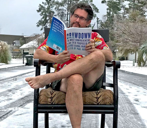 A man browses Drawdown sitting outside in the snow while barefoot and wearing shorts.